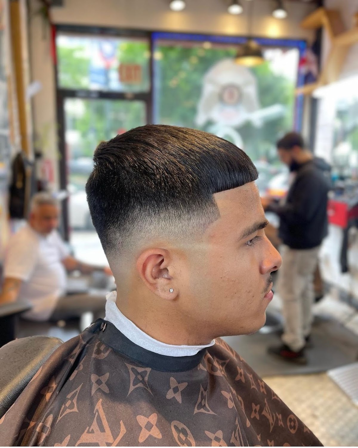 Side profile of a sharp skin fade with pompadour top, in a Louis Vuitton print cape