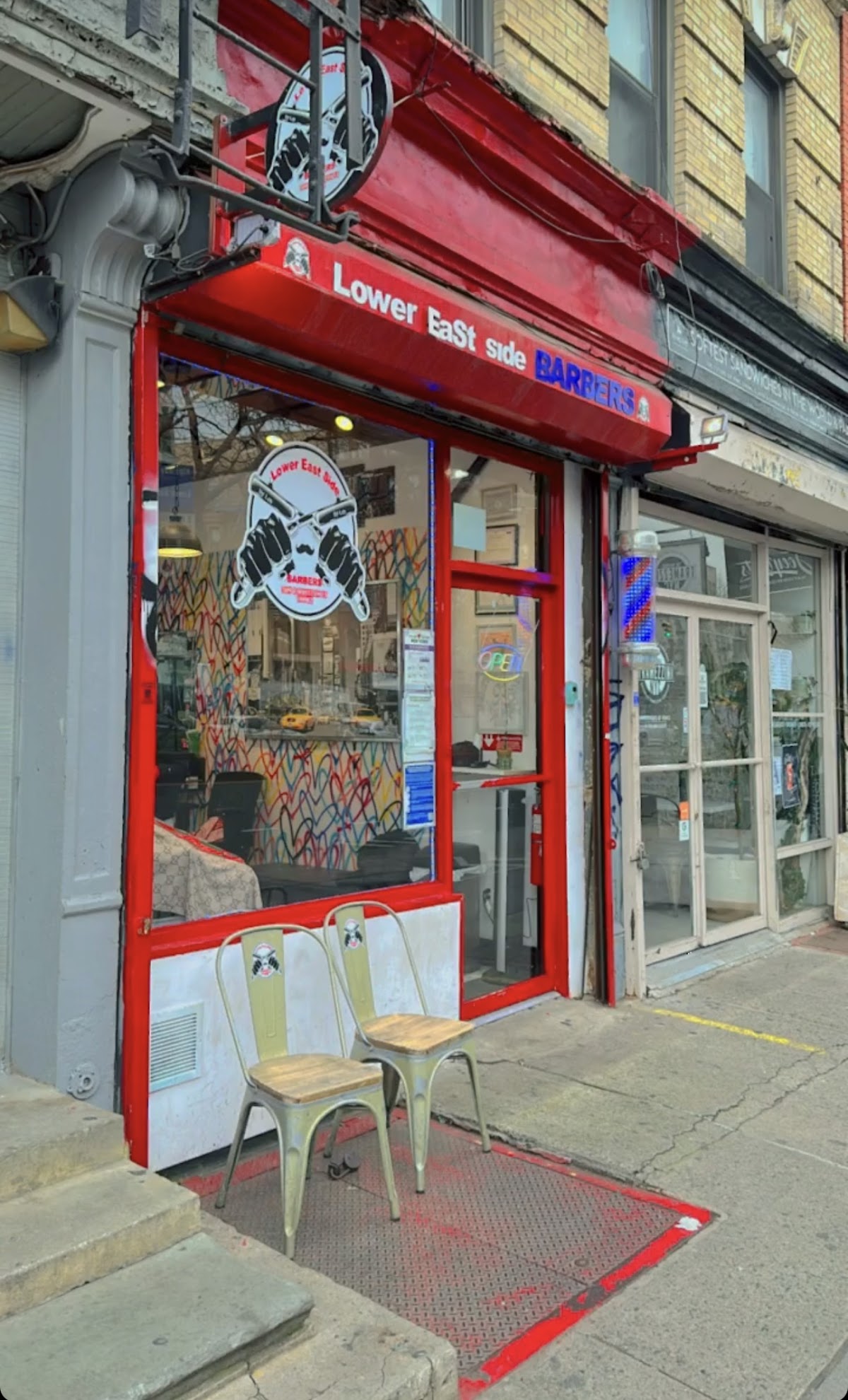 Lower East Side Barbers storefront on East Houston Street, red awning, LES Barbers logo on door, stools out front