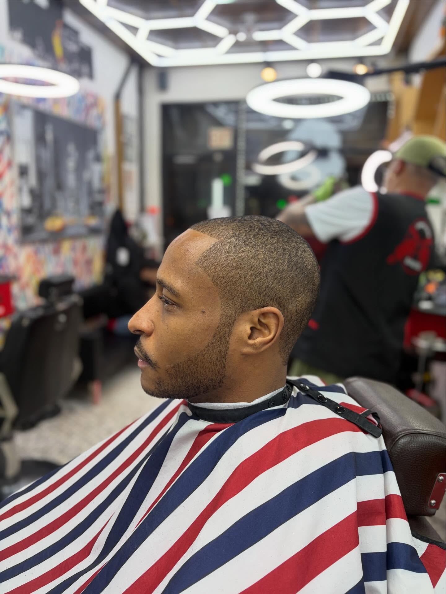 Side profile of a low fade with sharp lineup, classic red white and blue striped cape