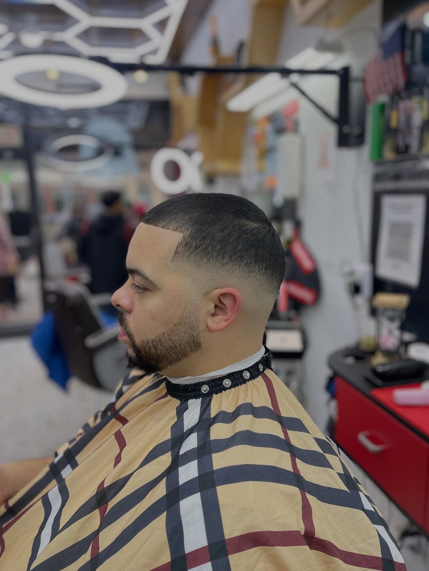 Sharp skin fade with crisp lineup, Burberry print cape, ring lights visible